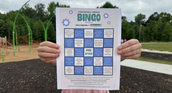 bingo board being held by two hands at a park with a playground in the background with cloudy skies