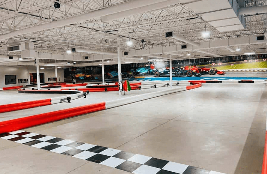 Photo taken from inside of K1 Speed, an indoor go-karting facility. Black and white checks line the beginning of the track with red and white bumpers surrounding the track.