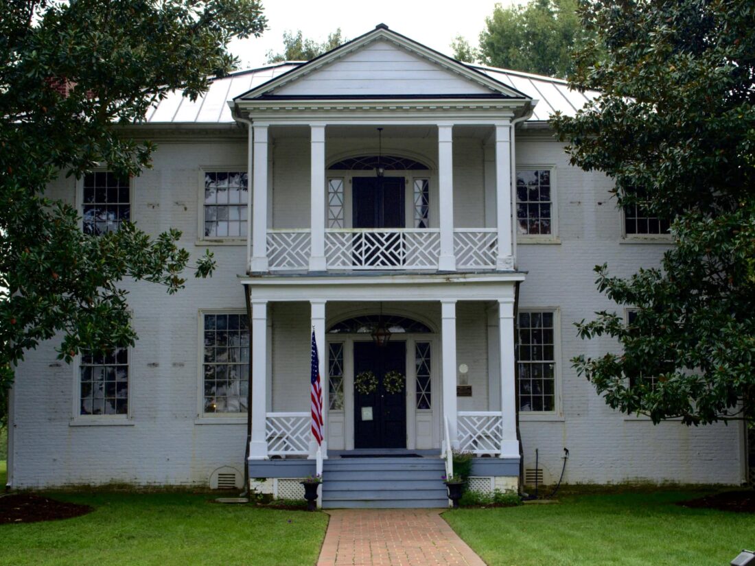 photo taken of Magnolia Grange, a historic white brick home built in the 1800s. The home features magnolia trees on either side and a balcony on the top level. 