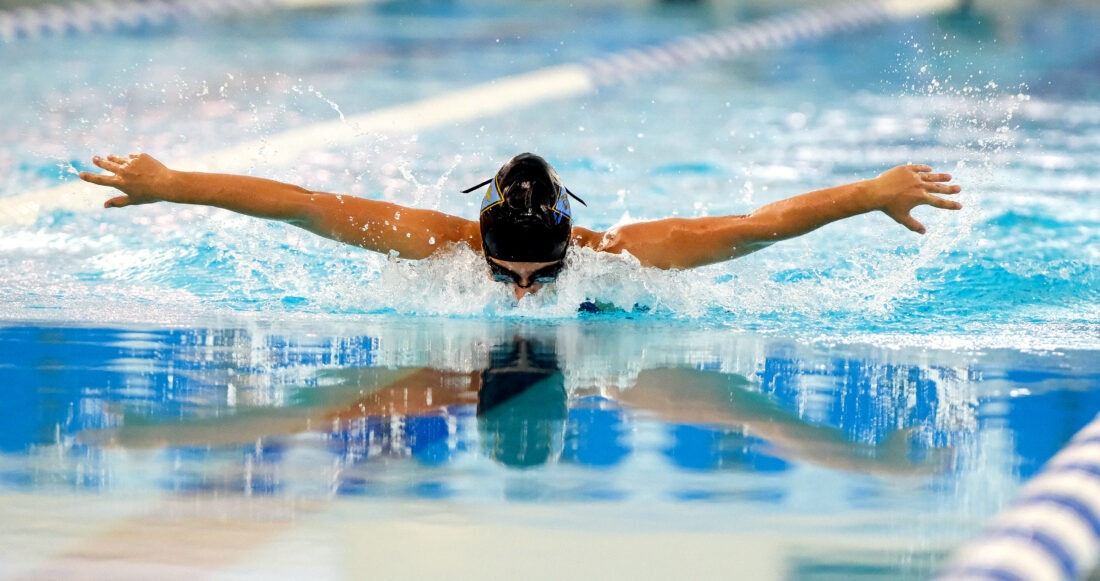 Up close photo of swimmer swimming the butterfly at SwimRVA. Swimmer has black swim cap on and goggles