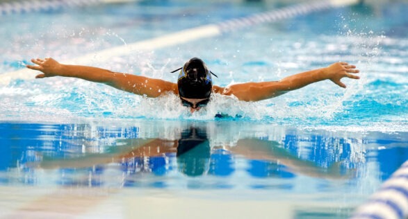 Swimmer swimming the butterfly at SwimRVA. Swimmer has black swim cap and goggles.