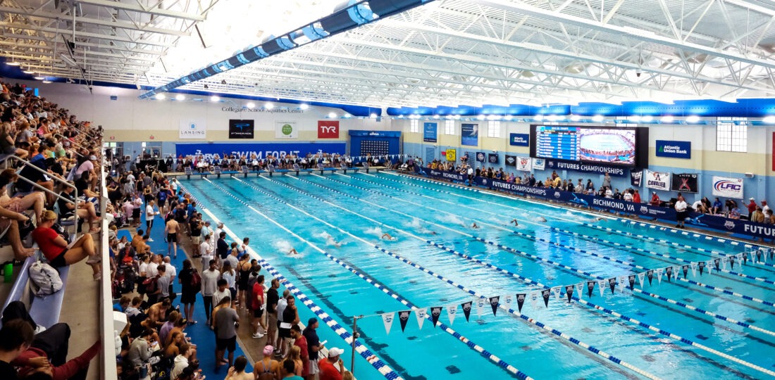 Large swimming pool located at SwimRVA with multiple lanes. Large crowd sitting in bleachers on the left side, overlooking the large pool.